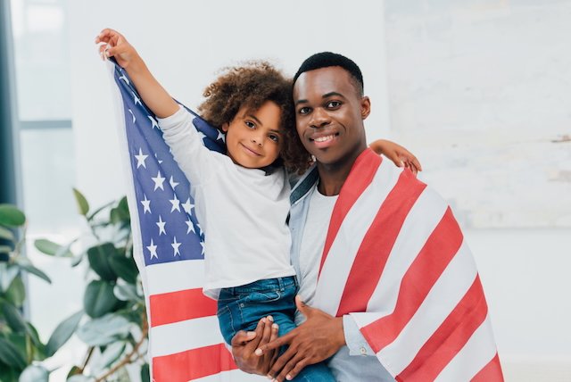 african american father and daughter wrapped in flag of america looking at camera